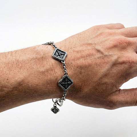 Close-up of a wrist wearing a silver bracelet with black square charms on a white background